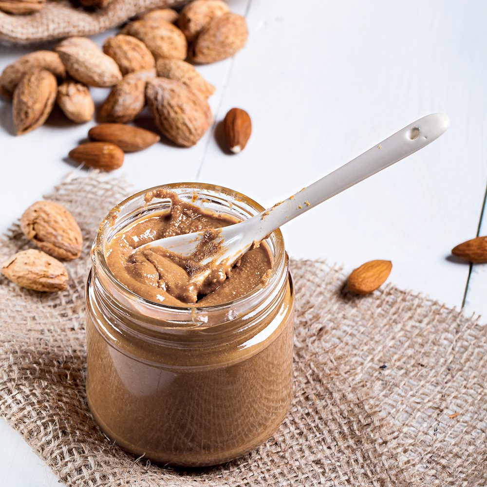 Homemade almond butter in a glass jar and a jute bag and napkin.